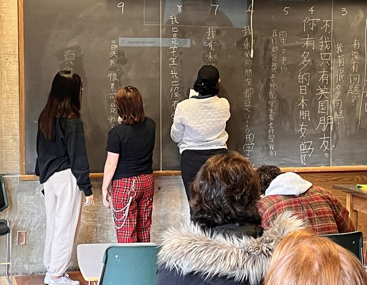 Students standing next to blackboard writing, Other students are taking notes