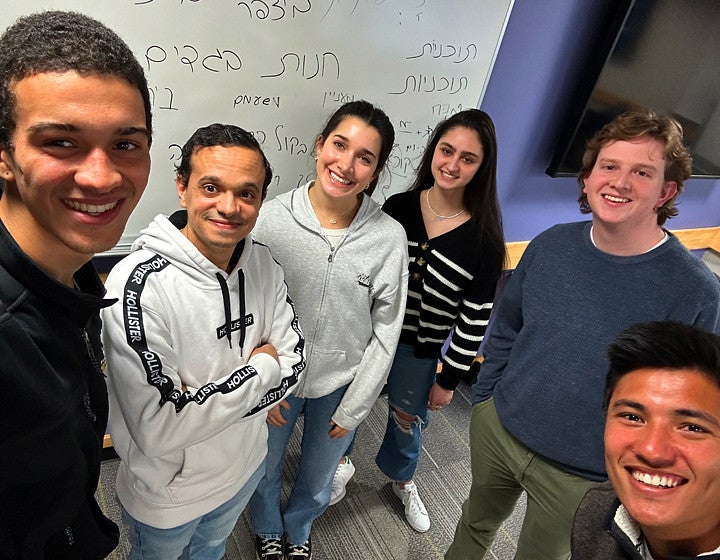 Group of students posing in front of a whiteboard with Hebrew letter on it