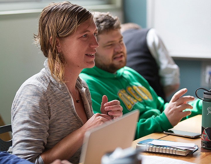 Two people sitting at a desk talking while looking at a laptop