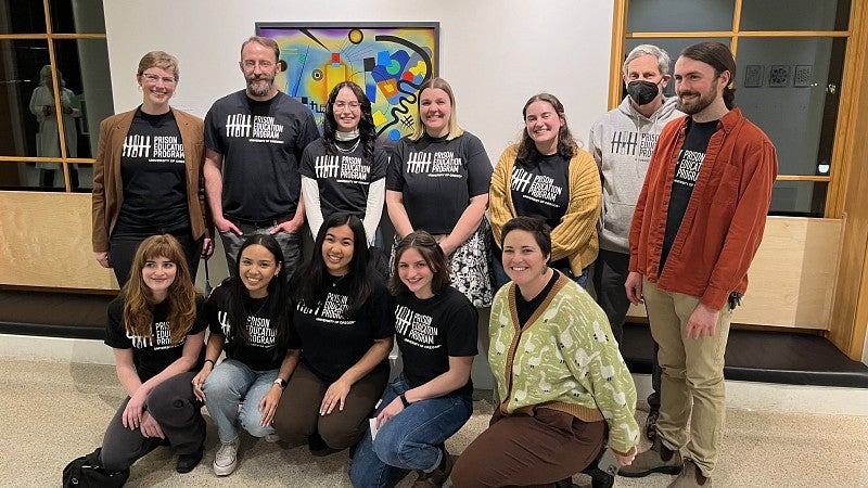 students in a group pose in a gallery setting wearing prison education system shirts