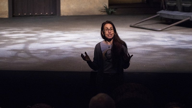 woman standing in front of stage addressing a crowd