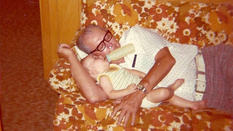 grandpa lying down on a couch holding a toddler drinking a bottle