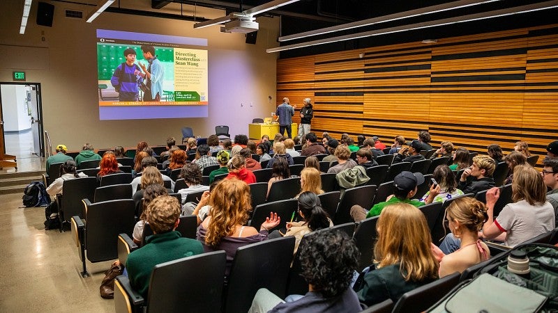 view from the back of a lecture filled with students looking at a screen