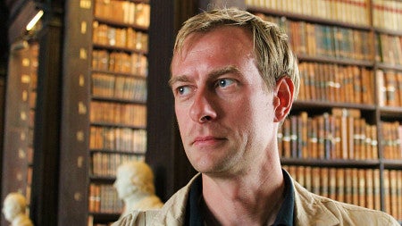 portrait of Colin Koopman posing in front of large bookshelves and marble busts