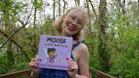 a student holds her book with a background of trees