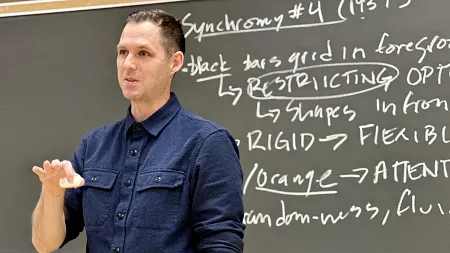 Colin Williamson stands in front of a blackboard, lecturing a class