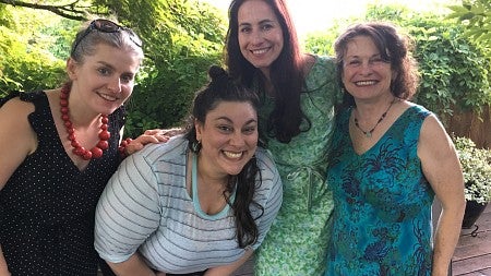 group of four women standing together outside smiling at the camera