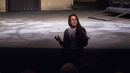woman standing in front of stage addressing a crowd