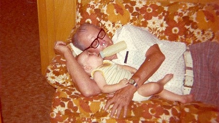 grandpa lying down on a couch holding a toddler drinking a bottle