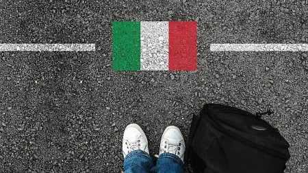 a man with shoes and backpack is standing on asphalt next to flag of italy and border