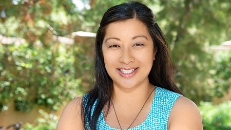 close up photo of woman smiling at the camera with trees behind her