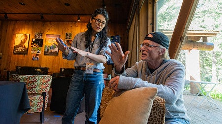 woman stands and uses hand gestures to demonstrate something to man sitting in a chair