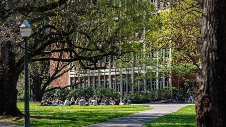 UO students sitting in circle on lawn on sunny day outside PLC Hall