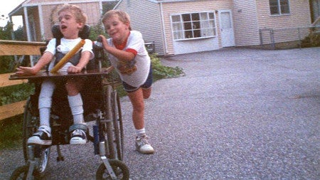 two young children, one in a wheelchair being pushed by the other