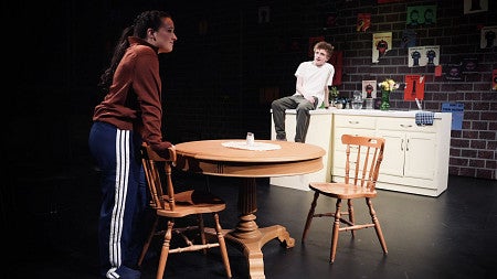 two actors standing are apart from each other on a stage that looks like an apartment