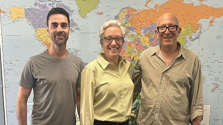 three people posed in front of a world map
