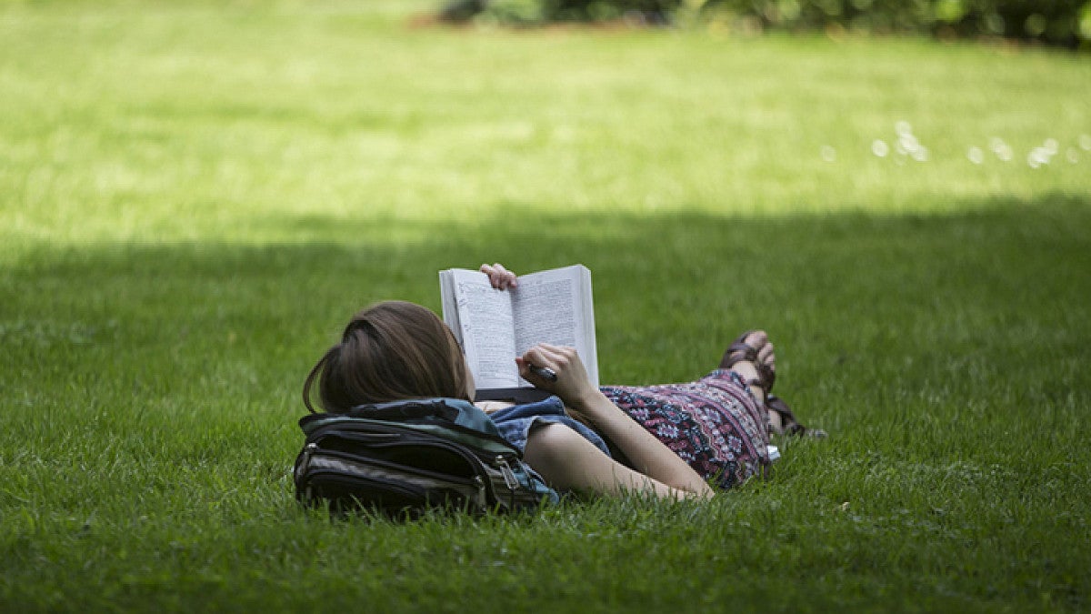 English Master's Degree (photo of student lying on grass reading a book)