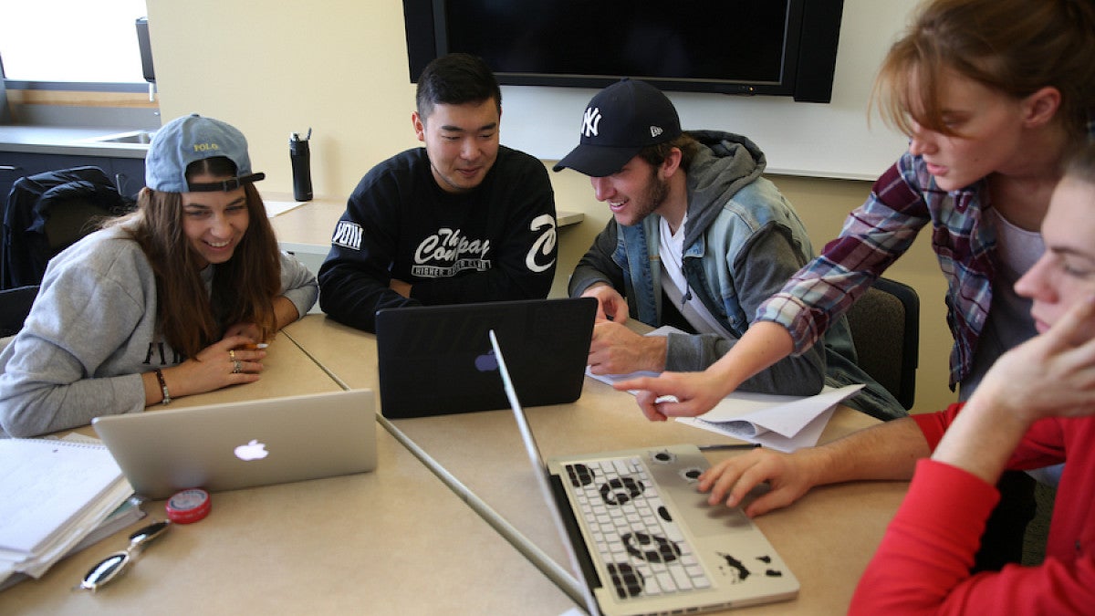 students at table with laptops talking