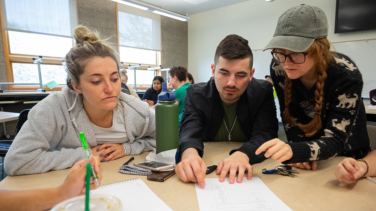 three students reading a document on the table