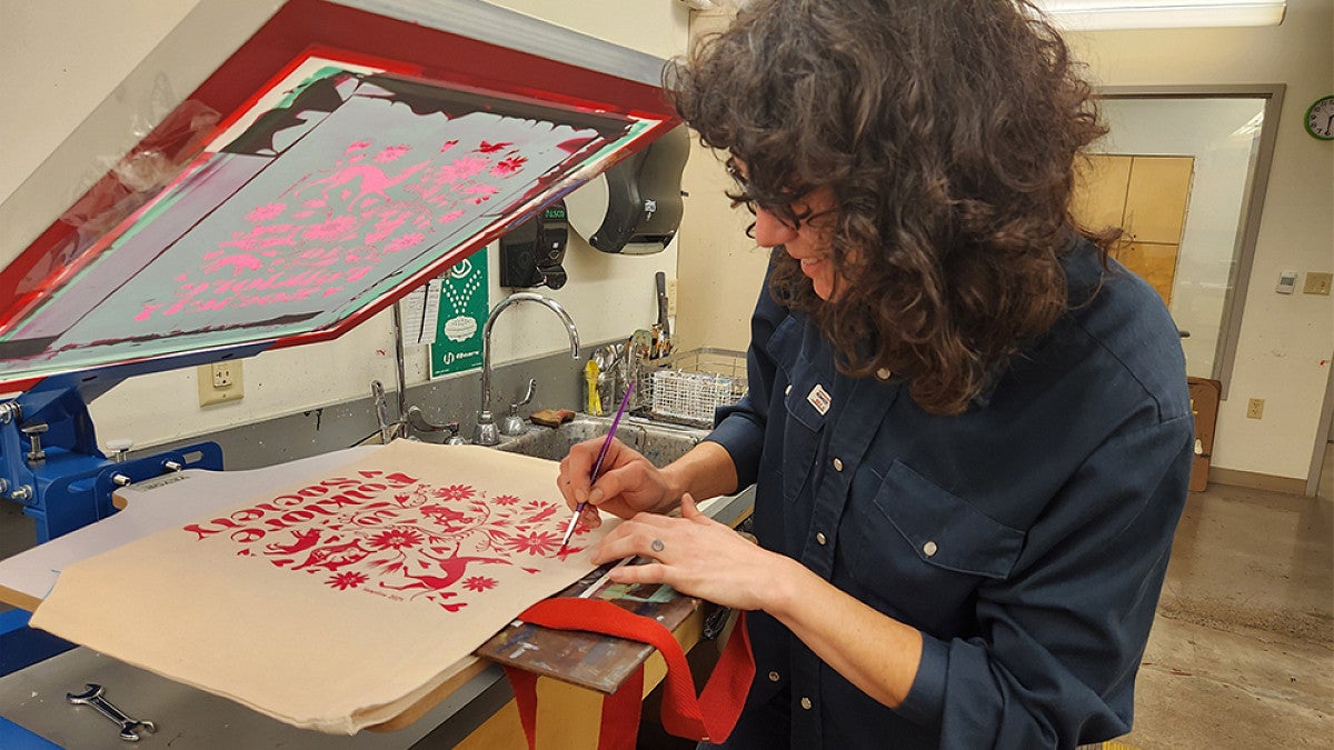 A student silk printing a design onto a canvas bag