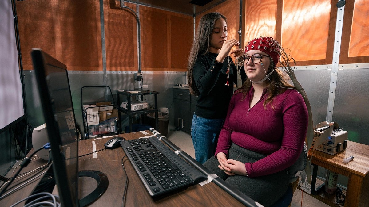 a person puts a dome shaped helmet on a student to track brain activity