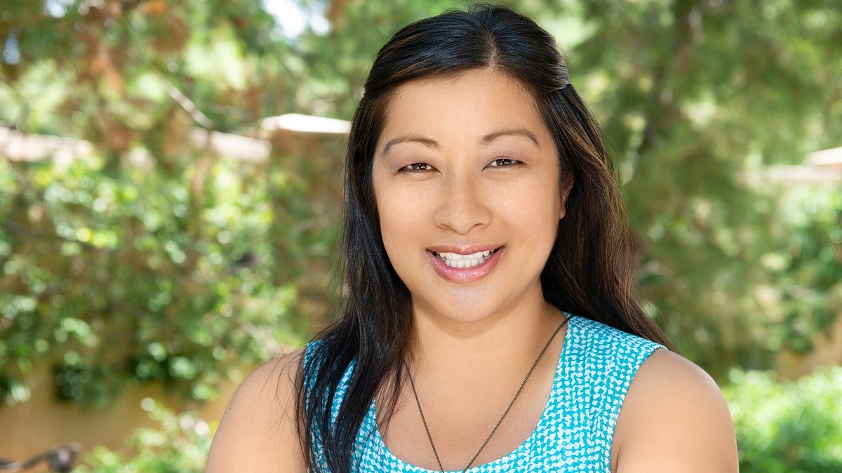 close up photo of woman smiling at the camera with trees behind her
