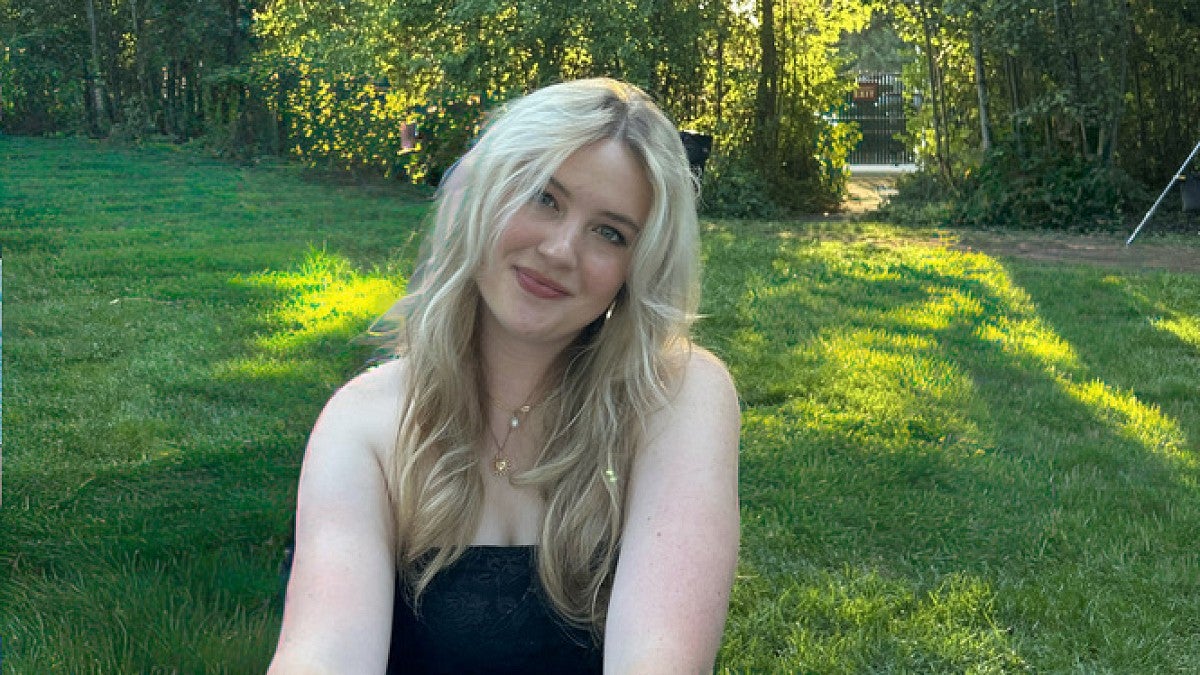woman smiling and sitting on the lawn with trees behind her
