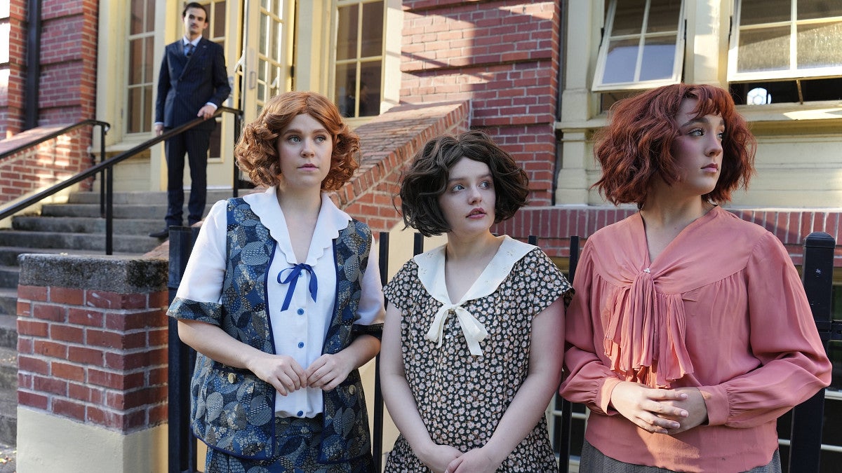 three women standing in front of a building with a may looming in the background