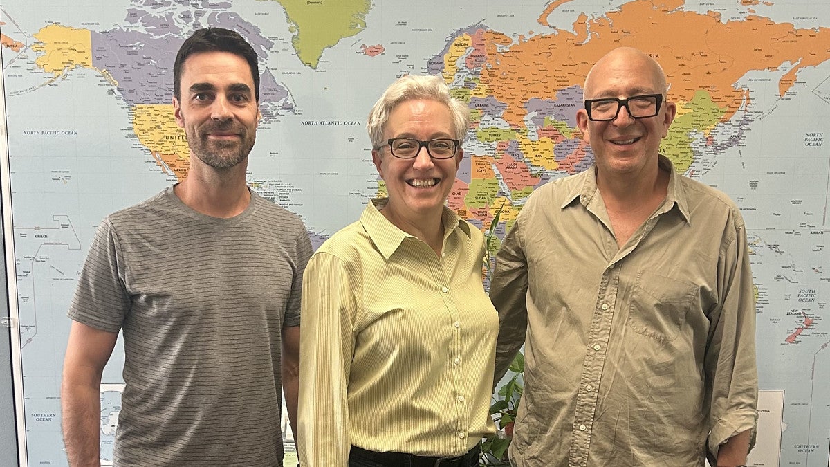 three people posed in front of a world map