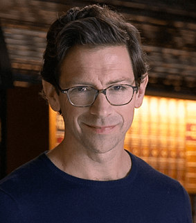 photo of man wearing glasses standing in a warmly lit library