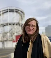 Photo of a woman wearing glasses in front of a roller coaster