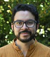 A man with glasses and a yellow shirt in front of trees