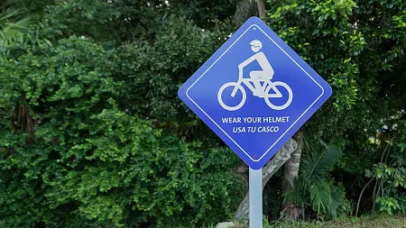 outdoor signpost with blue sign depicting a person on a bike and reading WEAR YOUR HELMET and USA TU CASCO
