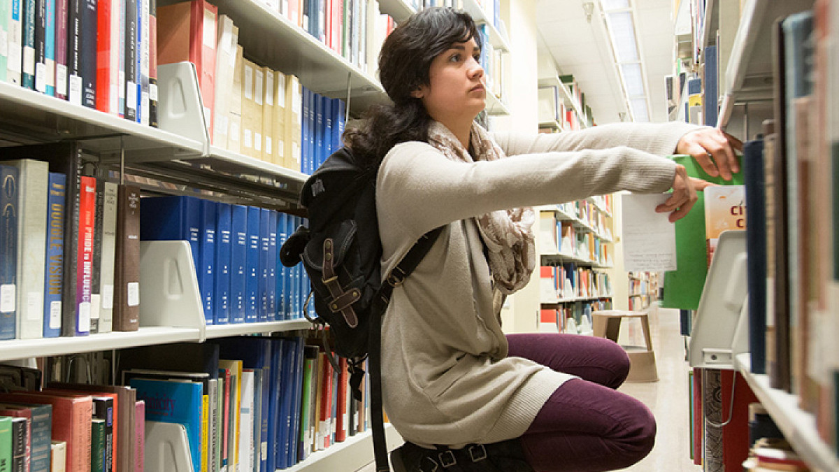 woman kneeling in library looking at books
